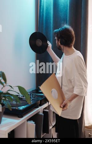 Homme tenant un disque vinyle à côté de la platine dans une chambre confortable Banque D'Images
