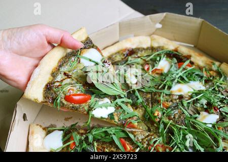 Cueillir à la main une tranche de pizza Arugula Balsamic dans une boîte en papier Banque D'Images