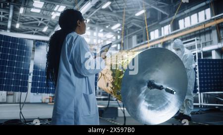 Femme ingénieur utilise une tablette numérique tout en travaillant sur la construction de satellites. Agence aérospatiale : scientifique supervisant la construction, l'assemblage et la fabrication d'engins spatiaux pour la mission spatiale Banque D'Images