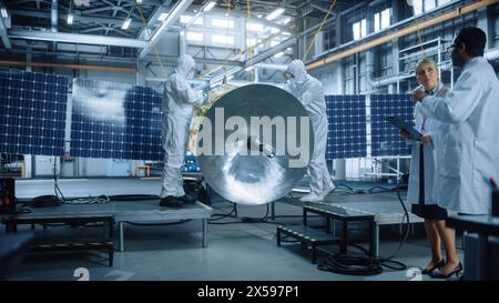 Ingénieur et technicien en combinaisons de protection travaillant sur la construction de satellites. Agence aérospatiale : équipe de scientifiques construisant des engins spatiaux pour l'exploration spatiale, la navigation, l'observation de la galaxie Banque D'Images