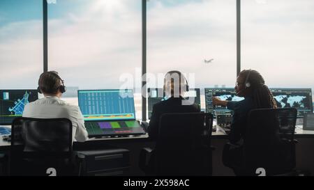 Équipe diversifiée de contrôle du trafic aérien travaillant dans une tour d'aéroport moderne. La salle de bureau est pleine d'écrans d'ordinateur de bureau avec écrans de navigation, données de départ et d'arrivée d'avion pour les contrôleurs. Banque D'Images