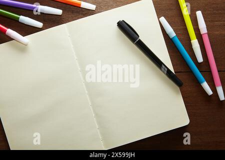 un carnet de croquis vide ouvert avec un marqueur noir et un certain nombre de marqueurs de couleur sur la table en bois Banque D'Images