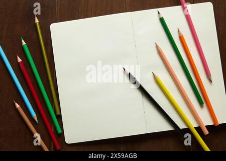 Un carnet de croquis vide est encore ouvert avec plusieurs crayons de couleur sur une table en bois Banque D'Images