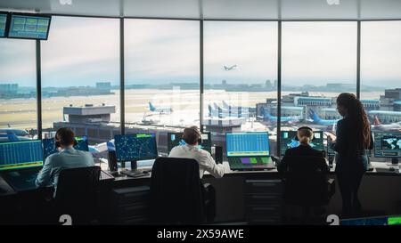 Équipe diversifiée de contrôle du trafic aérien travaillant dans une tour d'aéroport moderne. La salle de bureau est pleine d'écrans d'ordinateur de bureau avec écrans de navigation, données de départ et d'arrivée d'avion pour les contrôleurs. Banque D'Images