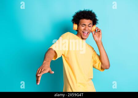 Photo de gars joyeux avec afro Hairdo t-shirt jaune habillé dans des écouteurs exécutant dj set isolé sur fond de couleur turquoise Banque D'Images