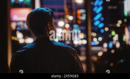 Bel homme marchant à travers Night City. Attrayant jeune homme voyageant, regardant autour du centre urbain contemplant des idées d'affaires, carrière future. Banque D'Images