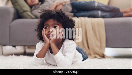 Penser, enfant et sol dans le salon avec idée, s'ennuyer ou se détendre sur le tapis en vacances scolaires. Jeune garçon, reposant et réfléchi avec la tête dans Banque D'Images