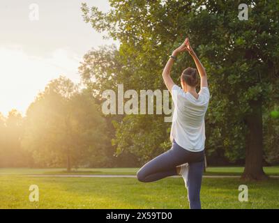 Jeune femme asiatique faisant du yoga le matin ou le soir au parc, femme en bonne santé se relaxant et pratiquant la pose d'arbre au parc de la ville. Pleine conscience, destinée, habitudes saines et concept d'équilibre Banque D'Images