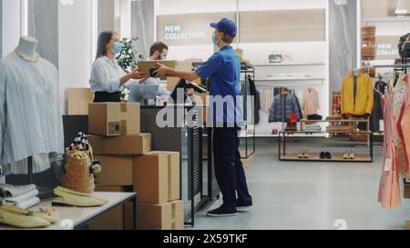 Comptoir de caisse de magasin de vêtements : les directeurs des ventes au détail femmes et hommes portant des masques de protection donnent le paquet à la personne de livraison de commande en ligne. Marques de créateurs disponibles à l'achat sur Internet Banque D'Images