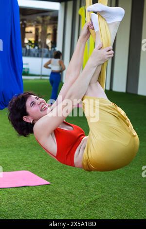 Une fille s'emmêle dans le tissu dans une pose amusante pendant le yoga aérien. Banque D'Images