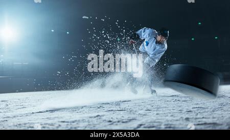 Patinoire de hockey sur glace : joueur professionnel tirant la balle avec bâton de hockey. Focus sur 3D Flying Puck avec effet Blur Motion. Grand angle spectaculaire, éclairage cinématographique. Banque D'Images