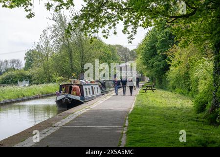 Petit groupe de personnes marchant vers la caméra le long d'un large chemin de halage le long duquel un certain nombre de bateaux étroits sont amarrés sur le système de canaux du Royaume-Uni. Banque D'Images