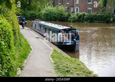 Trois hommes sont assis sur la proue de leur bateau étroit loué amarré sur le canal Llangollen à Ellesmere, Shropshire, mangeant et buvant. Banque D'Images