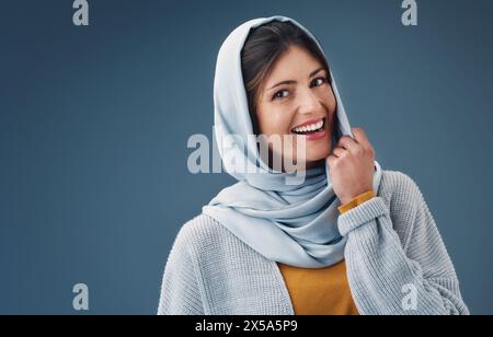 Femme, studio et sourire avec hijab en portrait avec heureux pour la confiance pour la culture islamique. Foi, beauté et fierté avec fond bleu pour arabe Banque D'Images