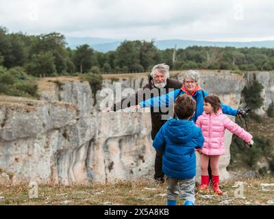 Une scène familiale réconfortante avec des grands-parents et leurs petits-enfants, un garçon et une fille, passant du temps de qualité ensemble dans un paysage naturel. Banque D'Images