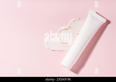 L'invention concerne une vue de dessus d'un tube cosmétique avec une crème pressée formant des formes de coeur sur une surface rose tendre, illustrant un texte crémeux d'un produit de soin de la peau Banque D'Images