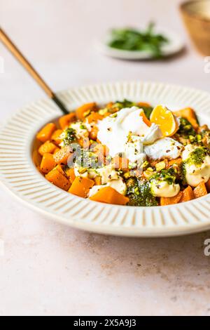 Image d'une assiette de courge rôtie surmontée de poupées de mayonnaise et de pesto vert arrosé, garnie de graines. Banque D'Images