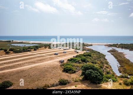 Vue aérienne panoramique de la côte en Sardaigne avec la plage de sable de Berchida, des véhicules, un parking et des arbustes méditerranéens par une journée ensoleillée Banque D'Images