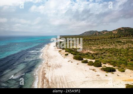 Vue aérienne d'une plage sereine de Berchida avec des eaux immaculées le long de la côte sarde, mettant en valeur un mélange de rives sablonneuses et de verdure luxuriante Banque D'Images