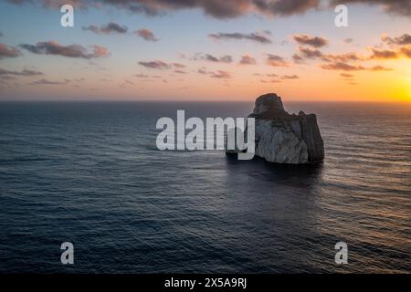 Coucher de soleil jette une lueur chaude sur une mer tranquille et une formation rocheuse majestueuse au large de la côte de Sardaigne, en Italie, encapsulant la beauté de la Méditerra Banque D'Images