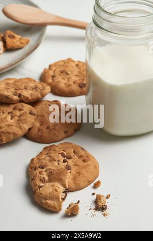Une vue de haut en bas d'une scène d'en-cas accueillante avec des biscuits aux pépites de chocolat et un pot de lait sur une surface blanche, incarnant une friandise réconfortante Banque D'Images