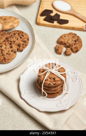 Une charmante présentation de biscuits aux pépites de chocolat, attachés avec de la ficelle sur une plaque blanche décorative, avec plus de biscuits et d'ingrédients à proximité Banque D'Images