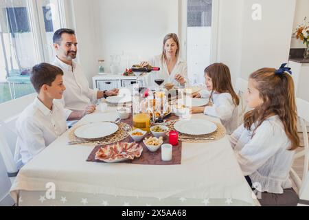 Une famille heureuse se réunit autour d'une table de Noël avec des décorations festives, profitant d'un repas et de la compagnie de l'autre à la maison Banque D'Images