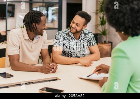 Trois professionnels ont une discussion amicale et collaborative dans un environnement d’espace de coworking moderne Banque D'Images