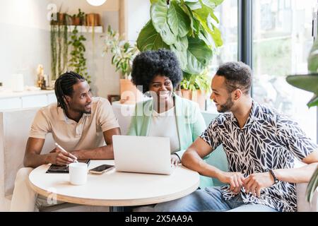 Un groupe diversifié de professionnels s'engagent dans des discussions autour d'un ordinateur portable dans un espace de coworking lumineux, illustrant le travail d'équipe et la collaboration dans un cadre décontracté Banque D'Images