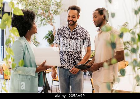 Un groupe diversifié de professionnels s’engagent dans une discussion tout en travaillant ensemble dans un environnement de coworking lumineux et rempli d’usines Banque D'Images