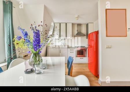 Comptoir avec évier et armoires blanches près du réfrigérateur rouge de style vintage dans la cuisine claire et élégante avec des appareils modernes et horloge dans l'appartement Banque D'Images