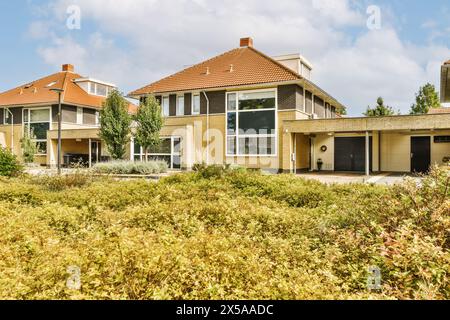 Maison moderne de banlieue avec un grand jardin, un garage double et de grandes fenêtres entourées de verdure par une journée ensoleillée. Banque D'Images