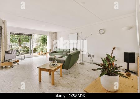 Un salon spacieux et moderne baigné de lumière naturelle, doté de canapés verts, d''une table en bois et offrant une vue sur le jardin par de grandes portes vitrées. Banque D'Images