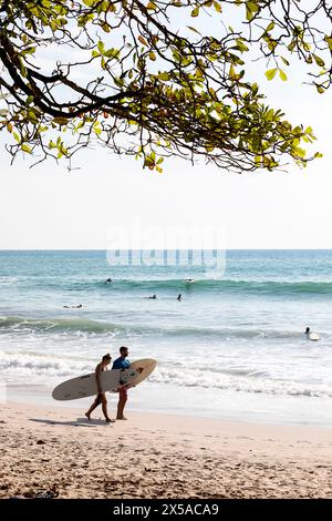 Surfeurs touristes avec des planches de surf dans leurs mains marchant sur une plage de sable de Santa Teresa, Playa Santa Teresa sur la péninsule de Nicoya au Costa rica Banque D'Images