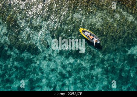 Une femme solitaire dans un chapeau de paille souriant, reposant couché flottant dans un kayak sur les vagues turquoises de la mer Adriatique. Vue aérienne du dessus de la côte. Exotique c Banque D'Images