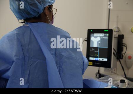 Infirmière surveillant le moniteur pendant l'administration d'un cathéter central inséré par voie périphérique (ligne Picc) administré sous anesthésie locale à l'hôpital Surrey E. Banque D'Images