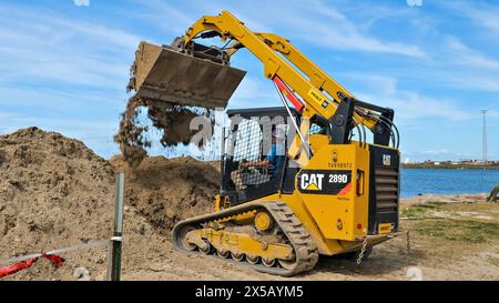 PORT ARANSAS, TX - 29 février 2020 : un ouvrier conduit une chargeuse frontale CAT 289D jaune pour vider une charge de saleté sur un chantier de construction près de l'ELAT Banque D'Images