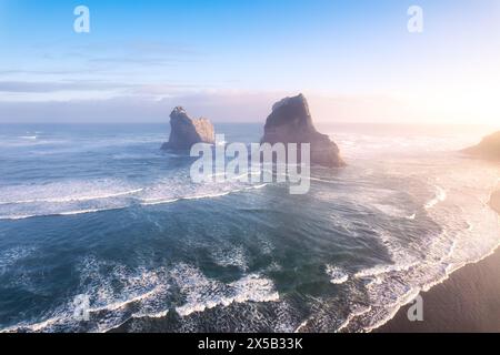 Vue aérienne du lever de soleil pittoresque qui brille sur la plage de Wharariki et l'île arcade sur la mer de Tasman à l'ouest de cape Farewell, Nouvelle-Zélande Banque D'Images