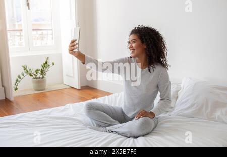 Femme assise sur le lit prenant Selfie après le réveil Banque D'Images