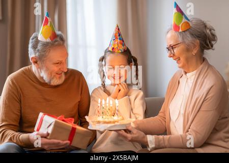 Joyeux grands-parents célébrant l'anniversaire des petites-filles avec gâteau et cadeau à l'intérieur Banque D'Images