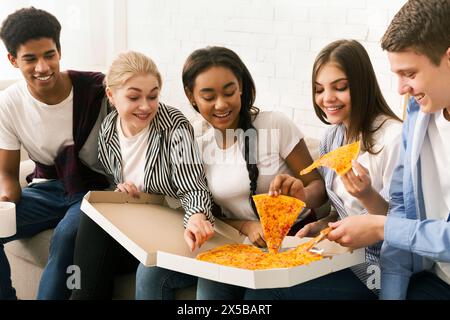 Groupe d'adolescents mangeant Pizza sur le canapé Banque D'Images
