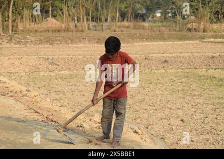 Travail juvénile au Bangladesh, un adolescent du petit village travaille avec tous les risques avec une pelle en acier tranchante et lourde dans une route rurale pour de l'argent. Banque D'Images