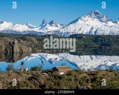 Le mont enneigé Cerro Castillo se reflète dans un lac, petite ferme au bord du lac, Patagonie, Chili Banque D'Images