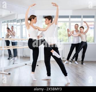 Heureuse femme souriante habillée en vêtements de sport noir et blanc appréciant la chorégraphie de ballet avec un partenaire masculin pendant la classe de groupe dans le salon de danse Banque D'Images