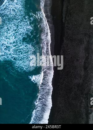 Vue aérienne de la plage islandaise de sable noir avec incroyable front de mer atlantique avec des vagues battantes. Scène froide dans le nord avec des montagnes enneigées et des rives sablonneuses avec du sable noir. Banque D'Images