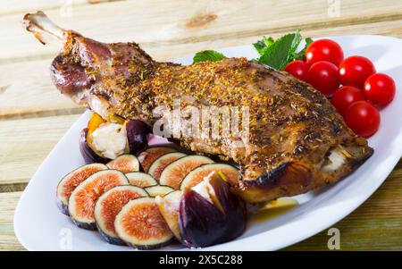 L'épaule d'agneau cuite au four est servie avec des figues, du fromage feta, des herbes et des tomates cerises à l'assiette Banque D'Images