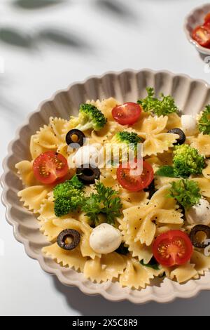 Salade de pâtes colorées avec farfalle, tomates cerises, olives, mozzarella, brocoli, et persil sur fond blanc Banque D'Images