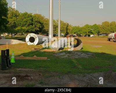 Vue large au-dessus de l'herbe verte section de poteau utilitaire en acier multiple posant le sol et l'eau camion et sous-station électrique à l'arrière. En fin d'après-midi. Ciel bleu Banque D'Images