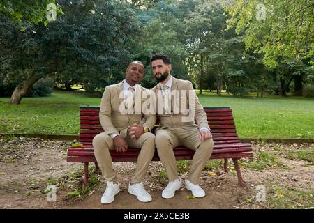 Plan général de deux hommes nouvellement mariés, souriant à la caméra, ils sont assis sur un banc en bois dans un jardin. Concept de bonheur, gay Pride Banque D'Images