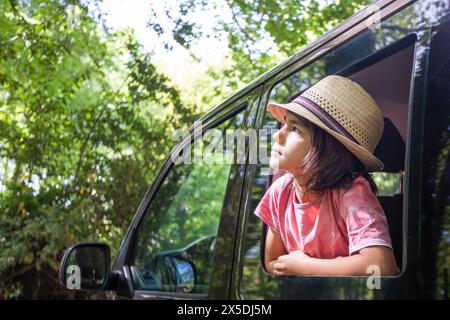 Un jeune garçon est assis dans une voiture avec son chapeau. Il regarde par la fenêtre et semble profiter de la vue Banque D'Images